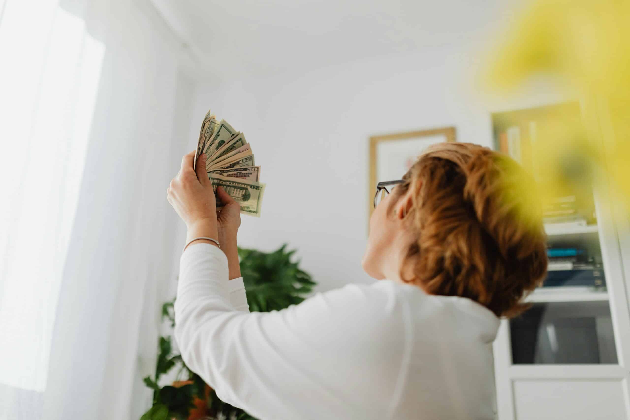 Finanzielle Unabhängigkeit: Definition und Bedeutung. Eine Frau hebt ihre Geldscheine in die Luft und freut sich
